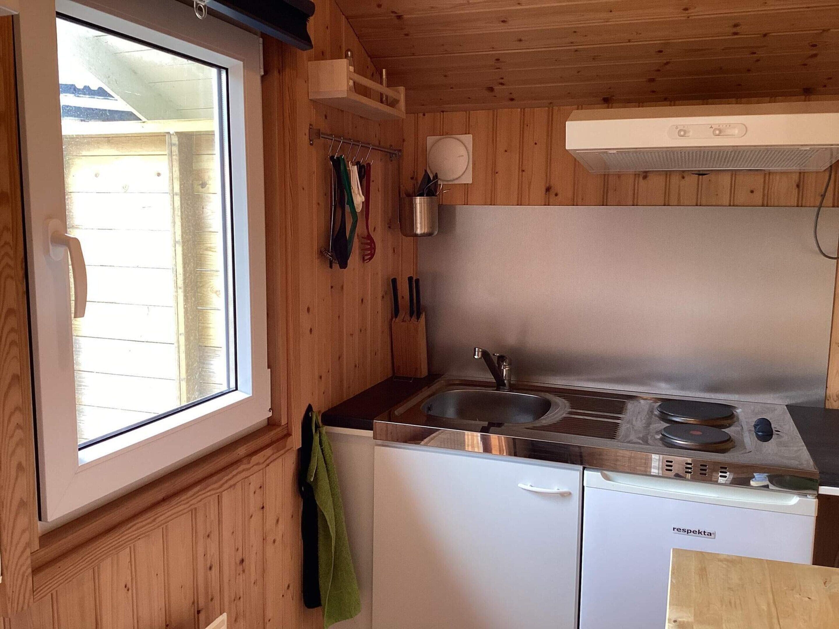 Una cocina compacta con ventana, paredes de madera, un lavamanos, una estufa y un lavavajillas.
