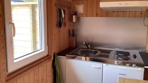A compact kitchen with a window, wooden walls, a sink, a stove, and a dishwasher.