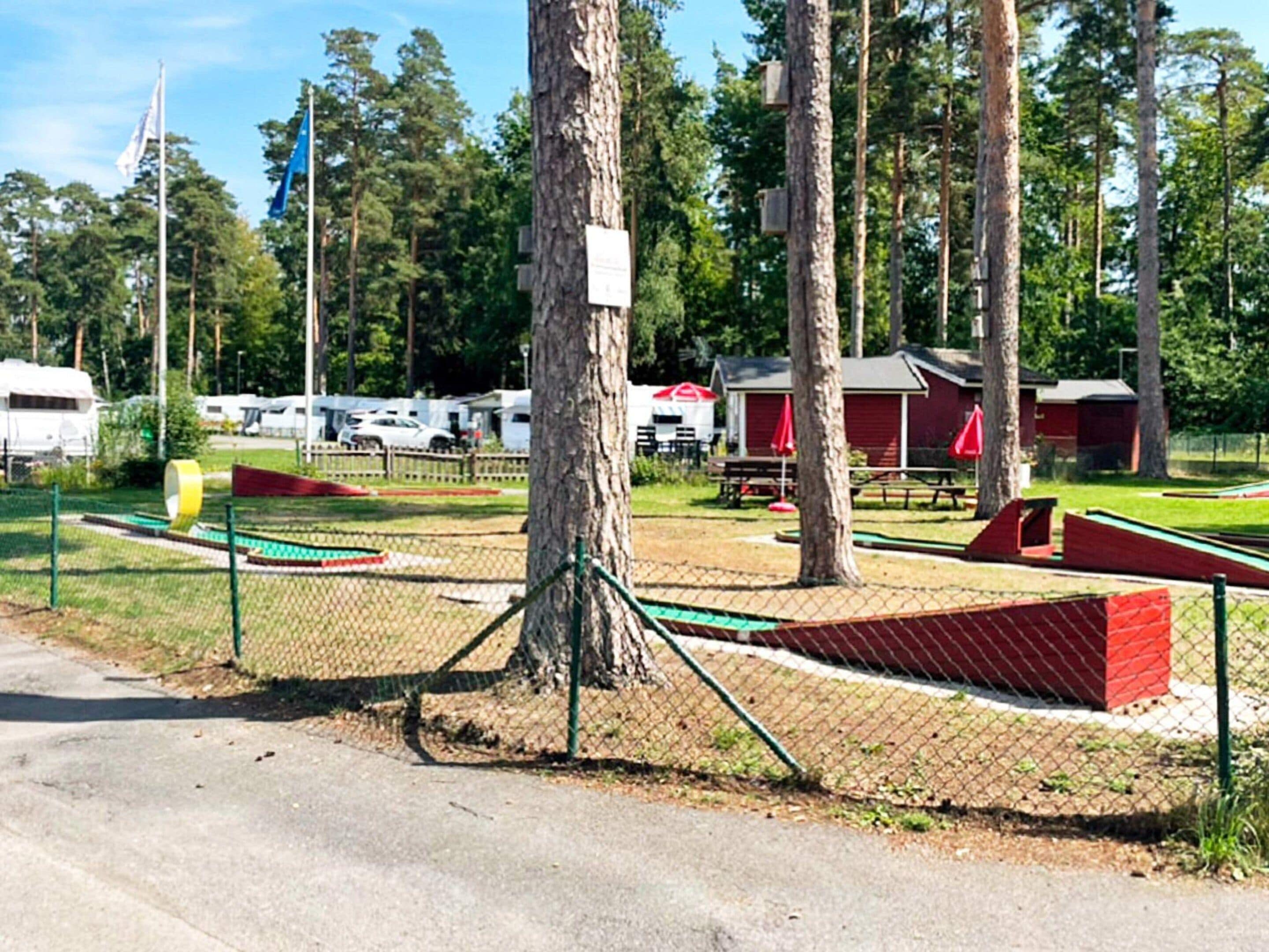 Un espacio al aire libre con mesas de picnic y un edificio rojo, delimitado por una cerca.