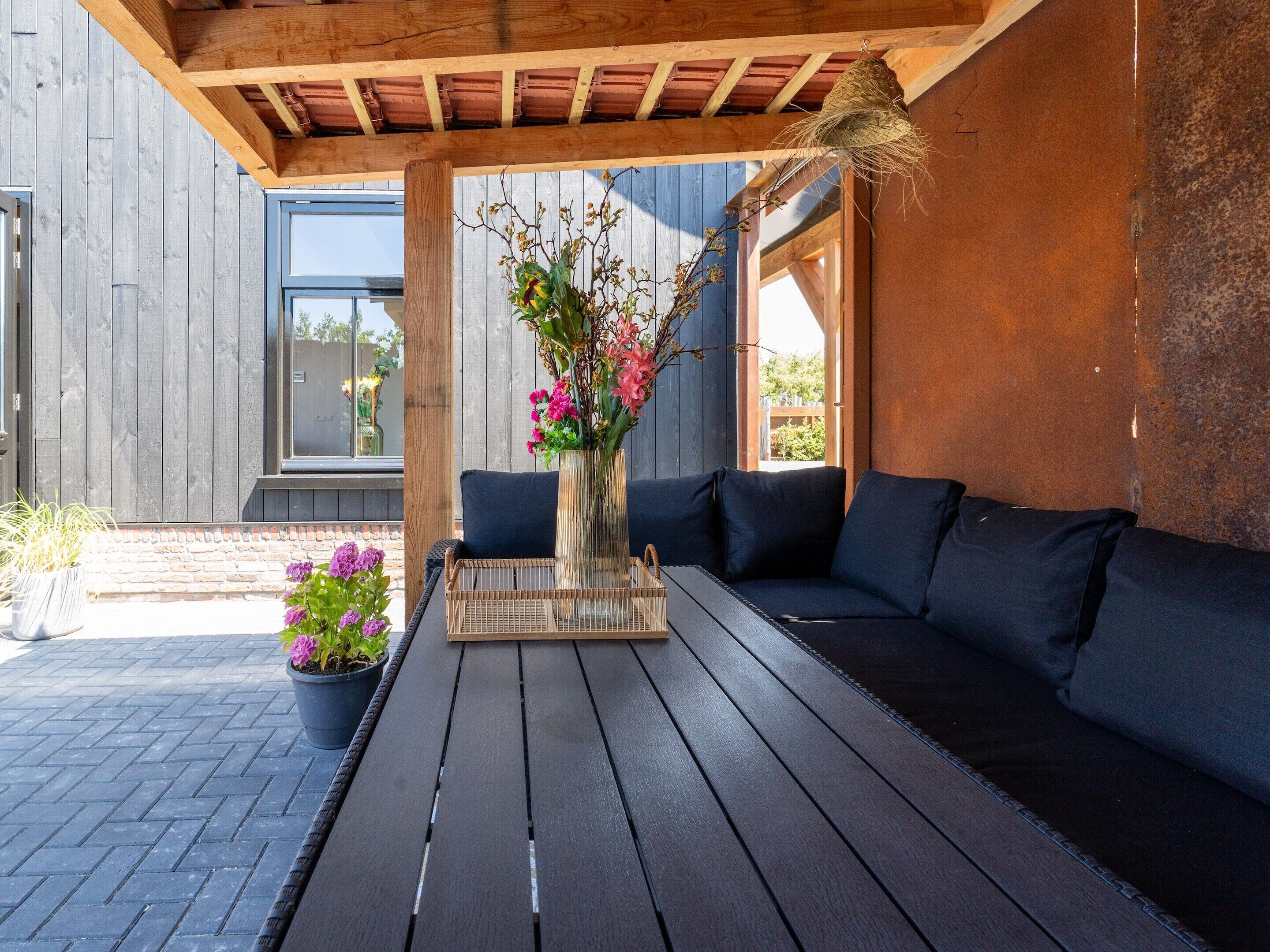 Un área de estar al aire libre, moderna, con una mesa de madera oscura, un sofá y un jarrón de flores.