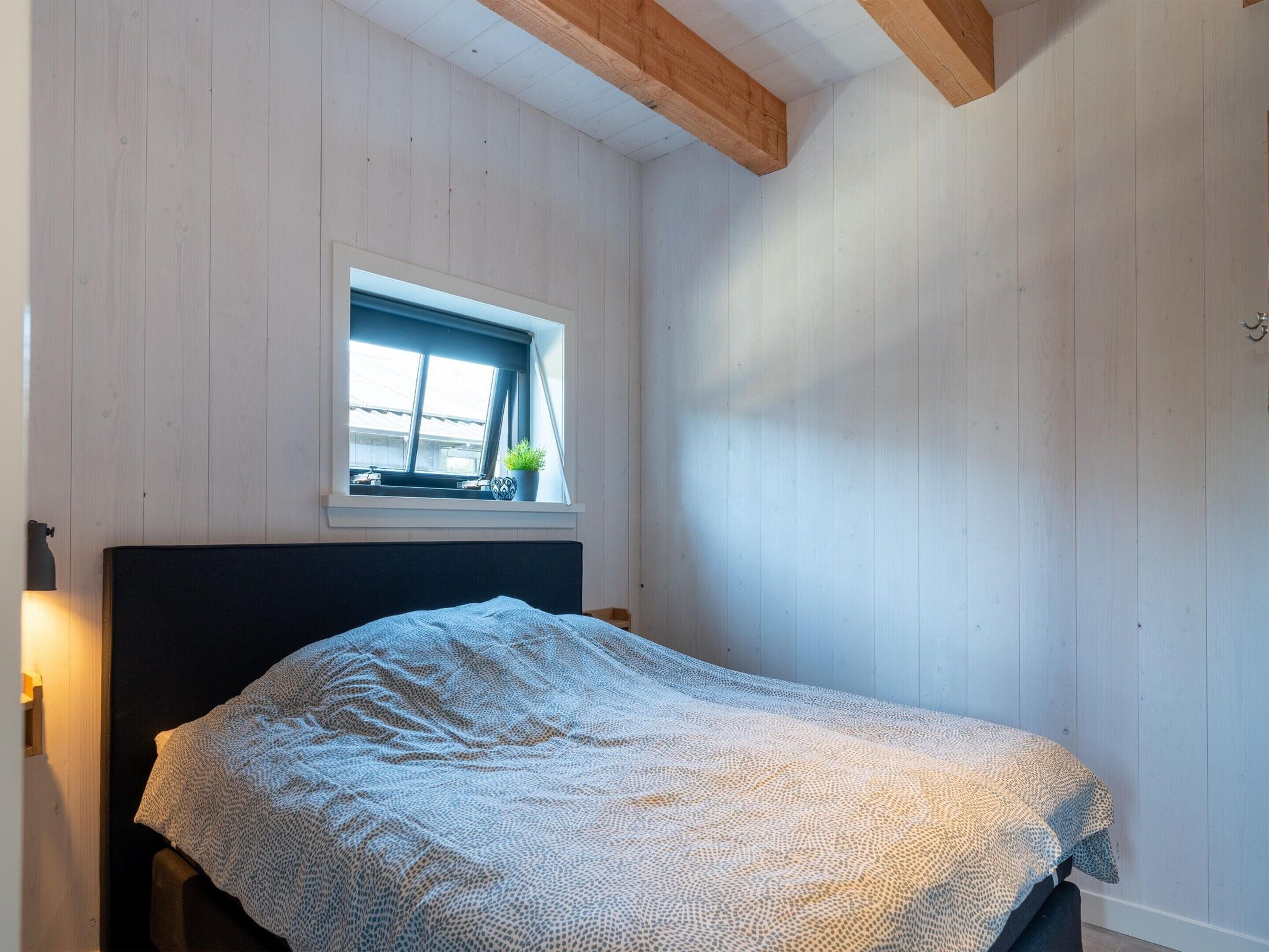 Een slaapkamer met een bed, een raam met uitzicht en een houten plafond.