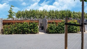 A paved outdoor area with a wooden fence and greenery.