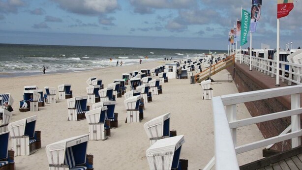 A beachside promenade with rows of white beach chairs and umbrellas, a wooden walkway, and flags. - Apartment in Ganzlin (Klanxbuell)