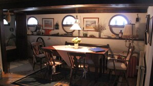 A cozy dining area with a wooden table, chairs, and a quilt on the floor. There are two windows with curtains, a lamp on the table, and a vase with flowers. - Apartment in Ganzlin (Klanxbuell)