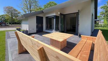 Une terrasse extérieure moderne, dotée de bancs en bois et d’une table, d’une porte-fenêtre coulissante et d’un petit espace jardin.