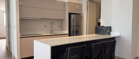 A modern kitchen with a central island, stainless steel appliances, and a bar area with chairs.