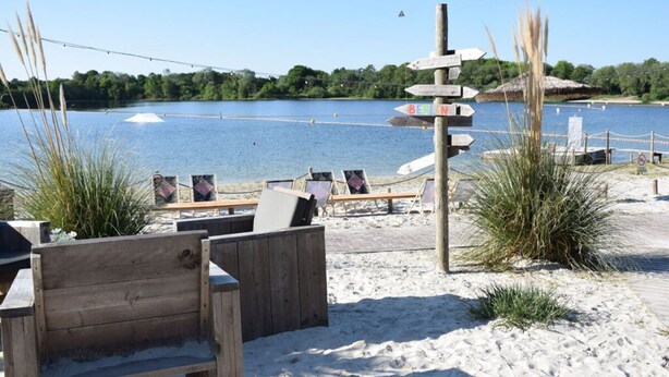 A beachside area with wooden benches and a signpost with directional arrows. - Holiday Home Maja am See (Aurich)