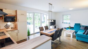 A modern apartment with a kitchen, dining area, and living room. It includes a microwave, stove, dining table, chairs, and a blue sofa. - Holiday Home Maja am See (Aurich)
