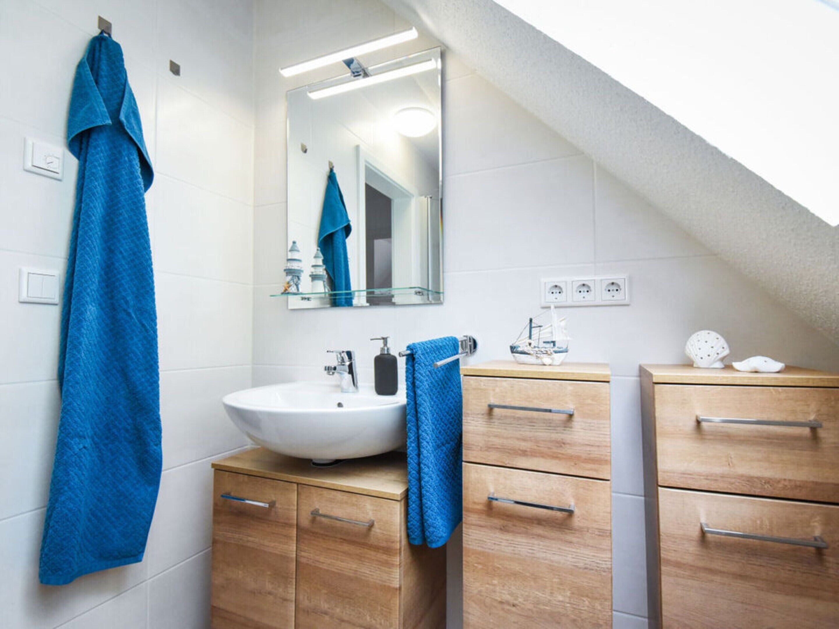 Un baño moderno con un lavabo blanco, un espejo y armarios de madera.