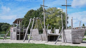 A wooden shipwreck structure with a lifebuoy and a small shelter. - Holiday Home Maja am See (Aurich)