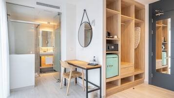 Una habitación de hotel moderna con kitchenette, una zona de comedor con mesa y sillas, un armario con varios compartimentos y un espejo en la pared.