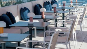 An outdoor seating area with tables and chairs, a sofa with cushions, and a large umbrella providing shade.