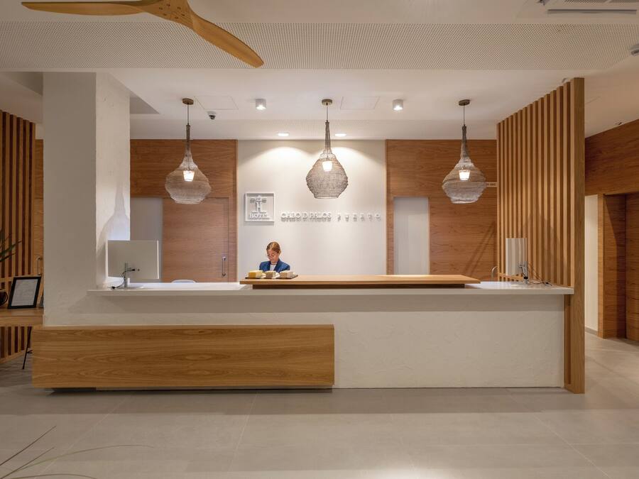 Un comptoir d’accueil d’hôtel avec un réceptionniste, des panneaux de bois et des luminaires suspendus.