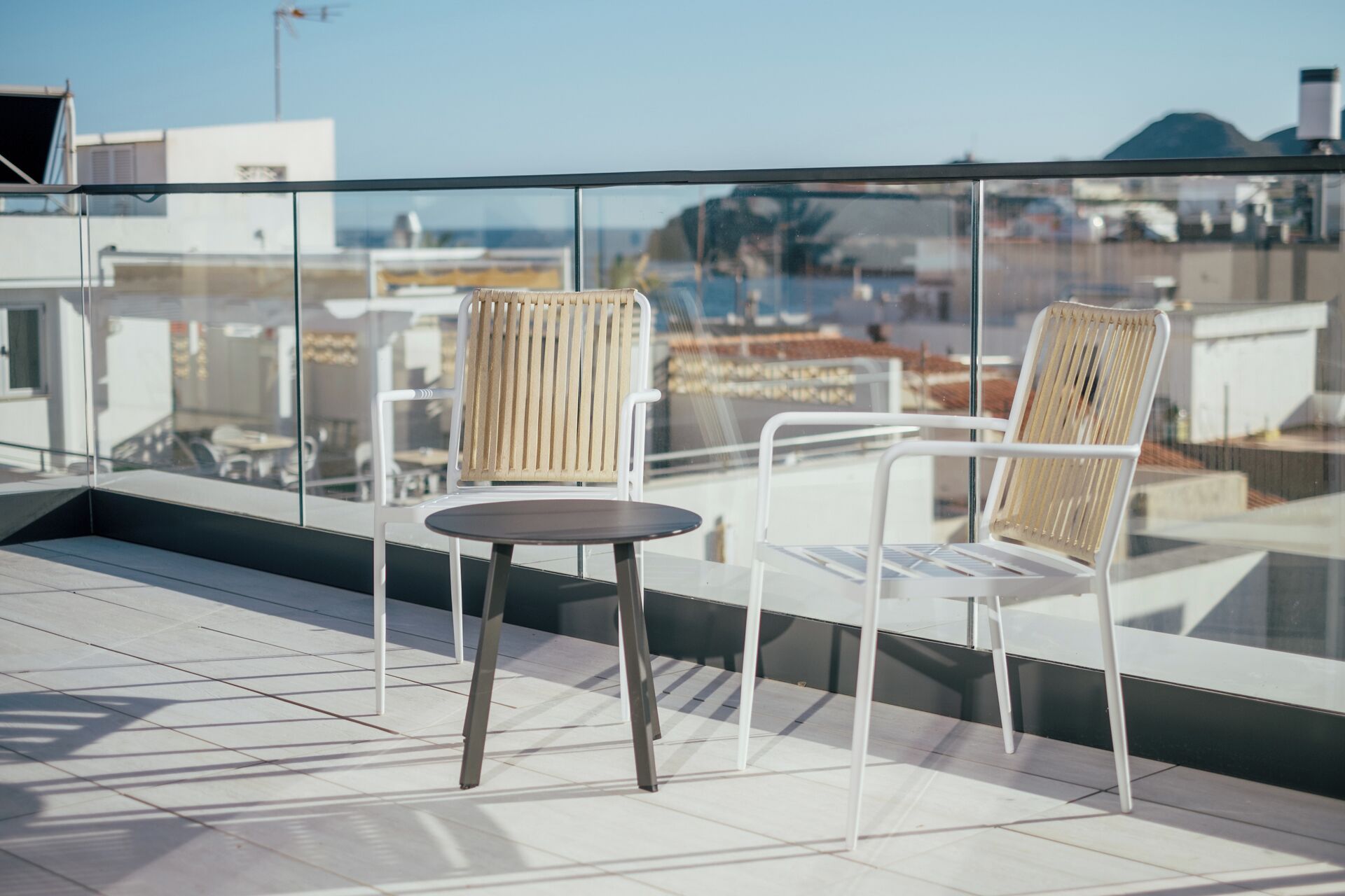 A rooftop terrace with two wicker chairs and a small table, overlooking a cityscape.