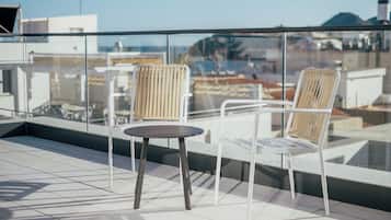A rooftop terrace with two wicker chairs and a small table, overlooking a cityscape.