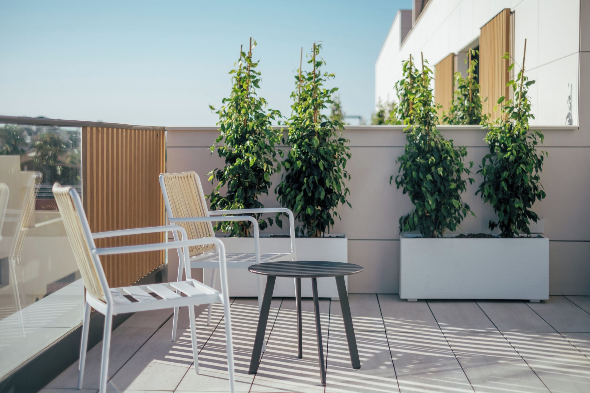 Een terras op het dak met twee witte stoelen, een kleine ronde tafel en potplanten.