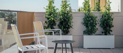 Una terraza en la azotea con dos sillas blancas, una mesa redonda pequeña y plantas en macetas.