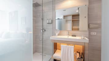 Un baño moderno con cabina de ducha de vidrio, tocador blanco con espejo y toallero.