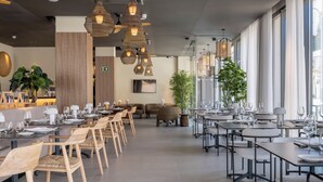 A modern restaurant with long tables, wicker chairs, and hanging light fixtures.