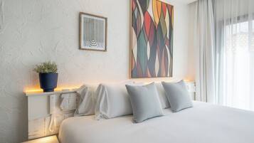 A modern hotel room with a large bed, a potted plant, and two artworks on the wall.