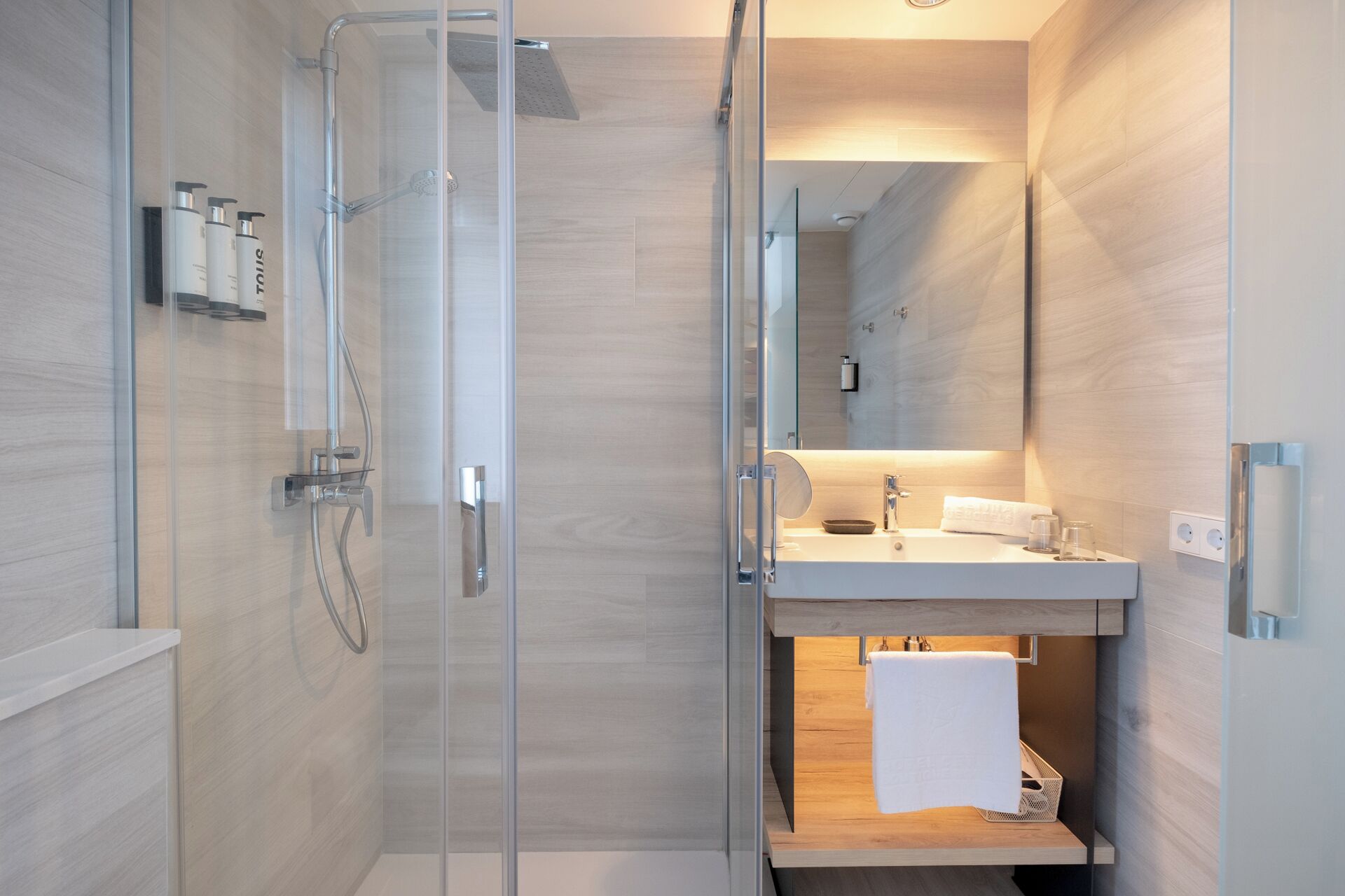 A modern bathroom with a glass-enclosed shower, a wooden vanity, and a mirror above the sink.