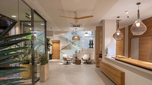A modern hotel lobby with a reception desk, seating area, staircase, and glass walls.