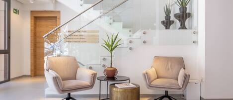 Un vestíbulo moderno con una escalera de cristal, dos sillones, una mesita redonda con una planta y una puerta de madera.