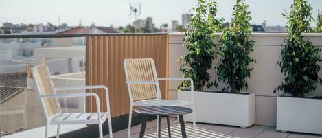 Une terrasse sur le toit, avec deux chaises et une table, entourée de plantes en pot.