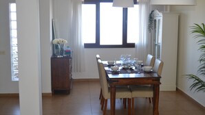 A dining area with a wooden table set for four, white chairs, and a vase of white flowers on a cabinet. - Casa Amplia y Espaciosa Para Descubrir un Tenerife Auténtico y Local (San Miguel)