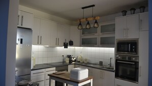 A modern kitchen with white cabinets, a built-in oven, a microwave, and a wooden table. - Casa Amplia y Espaciosa Para Descubrir un Tenerife Auténtico y Local (San Miguel)