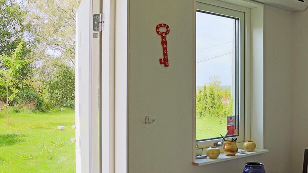 A room with a window overlooking a grassy area, a table with chairs, and a shelf with decorative items. - 4 Person Holiday Home in Onsala (Gottskar)