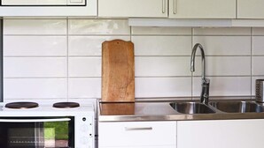 A kitchen with white cabinets, a microwave, a stove, a wooden cutting board, and a stainless steel sink. - 4 Person Holiday Home in Onsala (Gottskar)