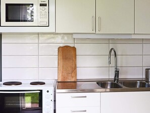 A kitchen with white cabinets, a microwave, a stove, a wooden cutting board, and a stainless steel sink. - 4 Person Holiday Home in Onsala (Gottskar)