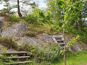 Un cadre naturel en plein air, avec un escalier en bois menant à une pente rocheuse, le tout entouré de verdure et d’arbres.