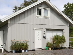 Il s’agit d’un bâtiment d’un seul étage, à l’extérieur blanc, avec une porte de garage et une petite fenêtre. On y trouve des plantes en pot et une échelle près de l’entrée.
