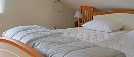 A single bed with a wooden frame and a white mattress, a wooden headboard, and a bedside table with a lamp.