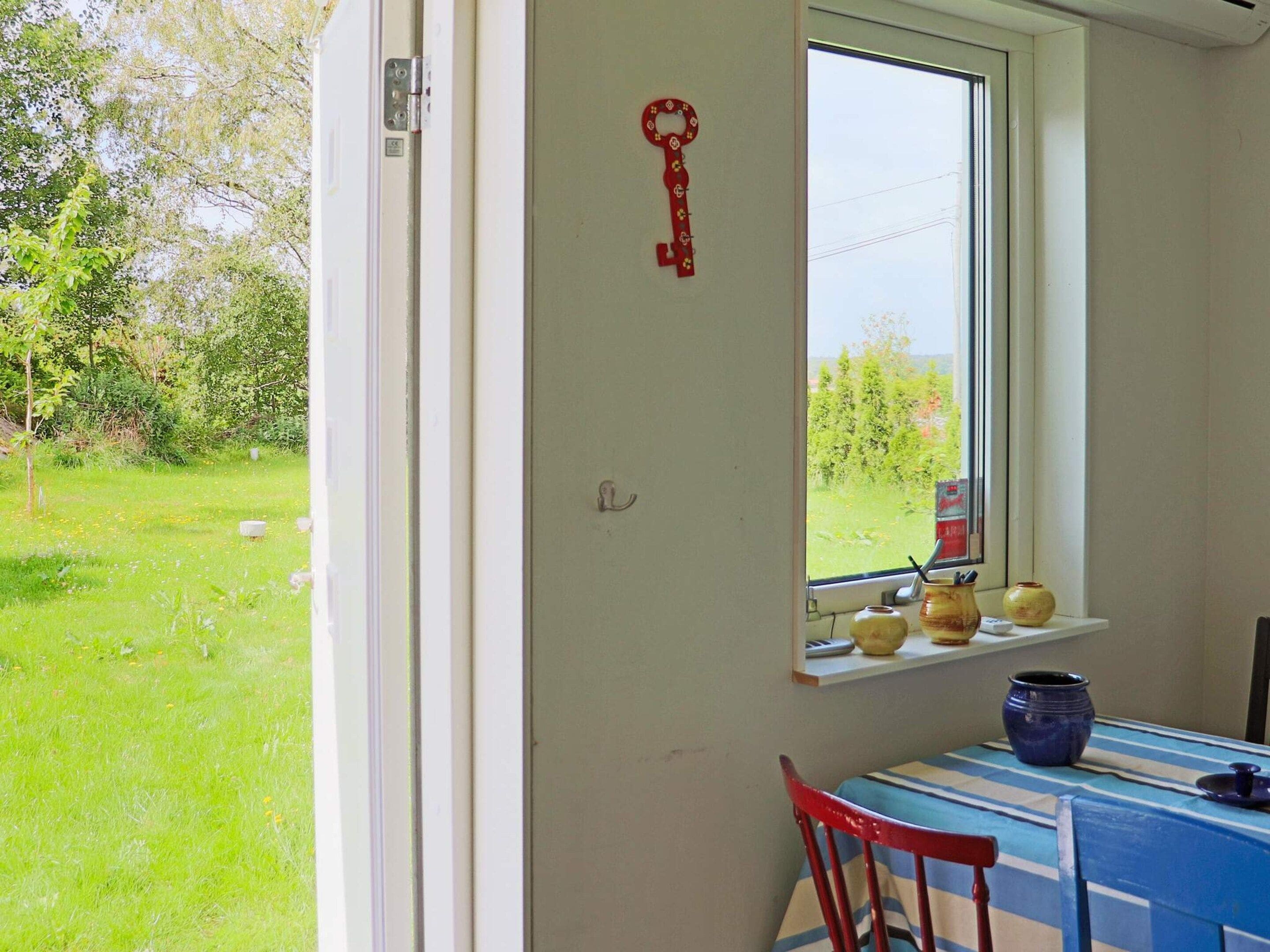 Una habitación con ventana que da a un jardín, una mesa con sillas y una estantería con adornos.
