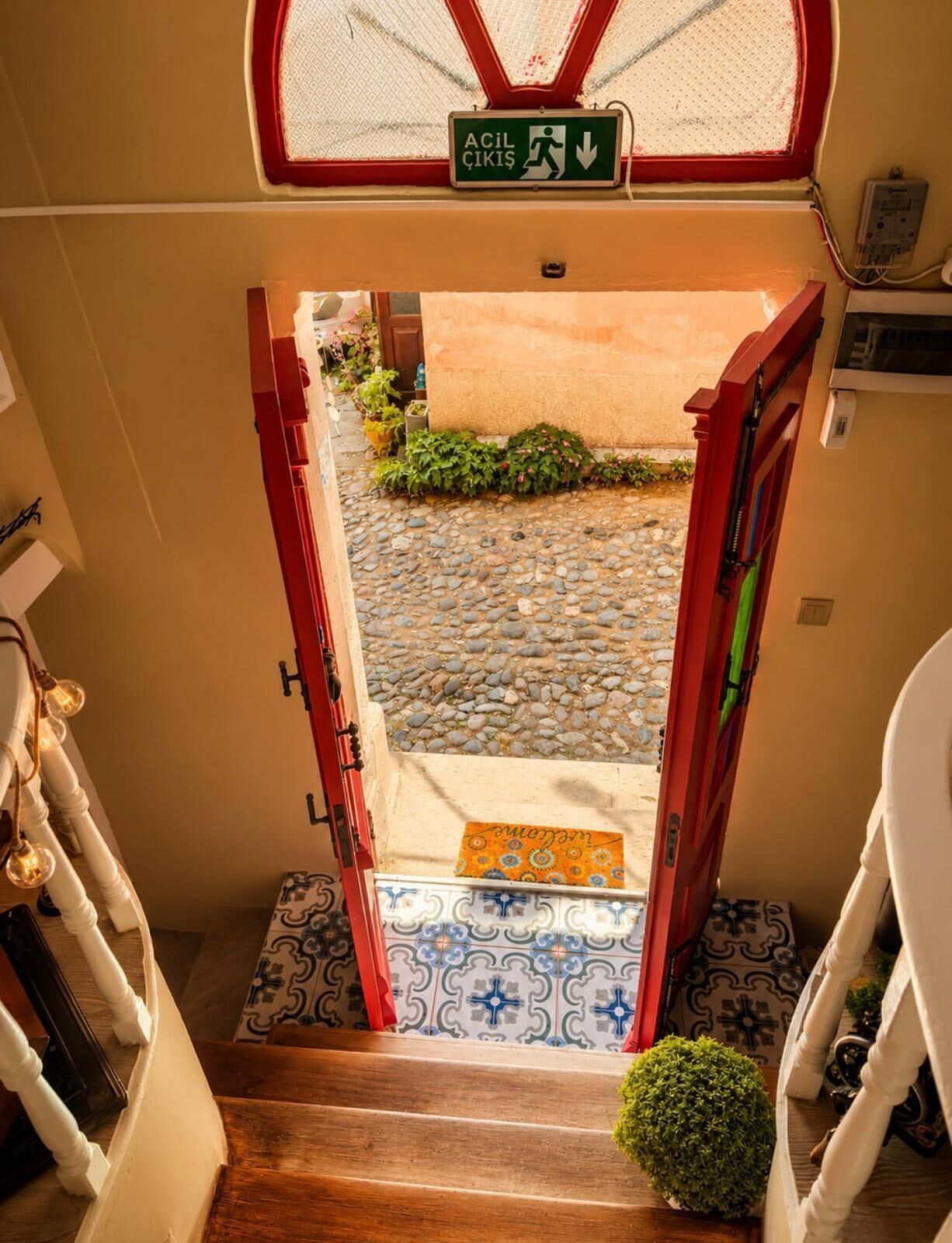 A staircase leading to a door with an emergency exit sign, a small potted plant, and patterned tiles.