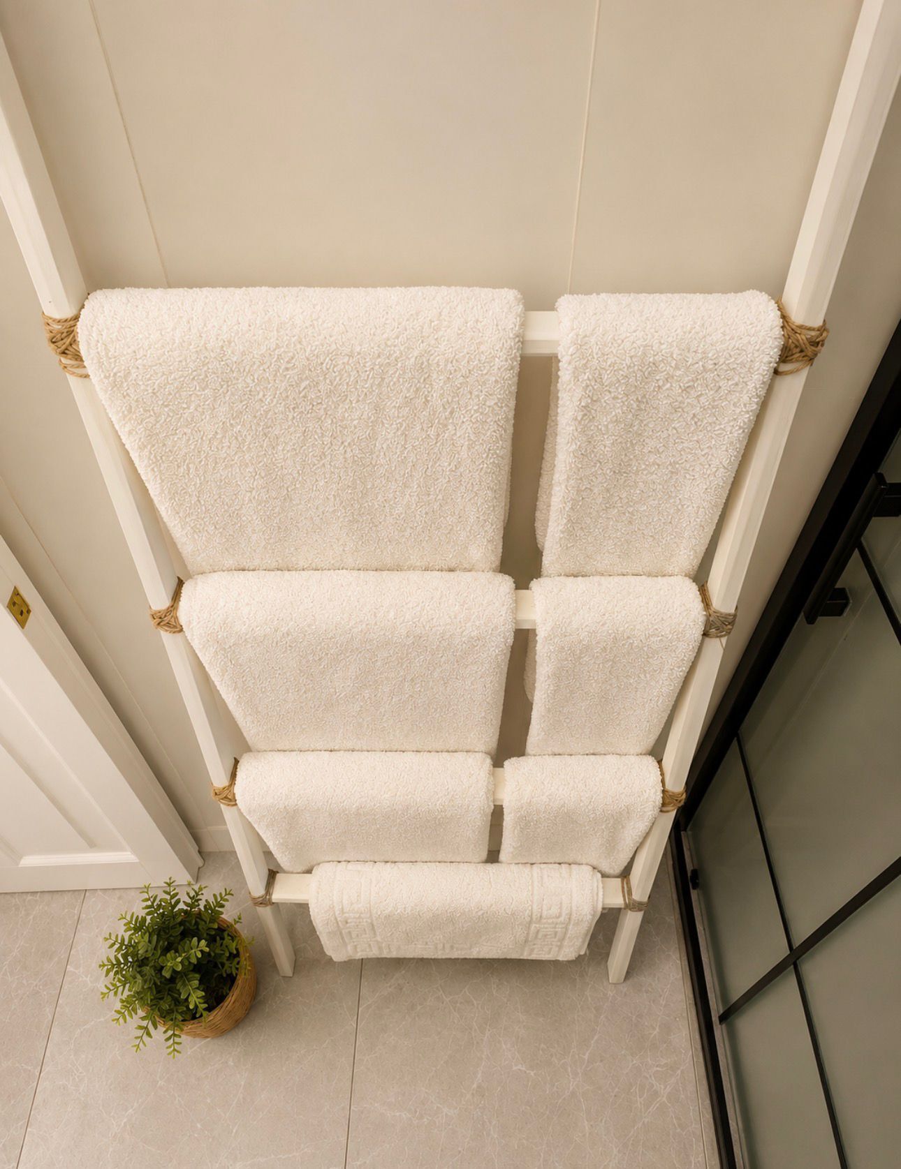 Silla blanca con textura y detalles de cuerda, ubicada frente a una pared con una planta en maceta cerca.