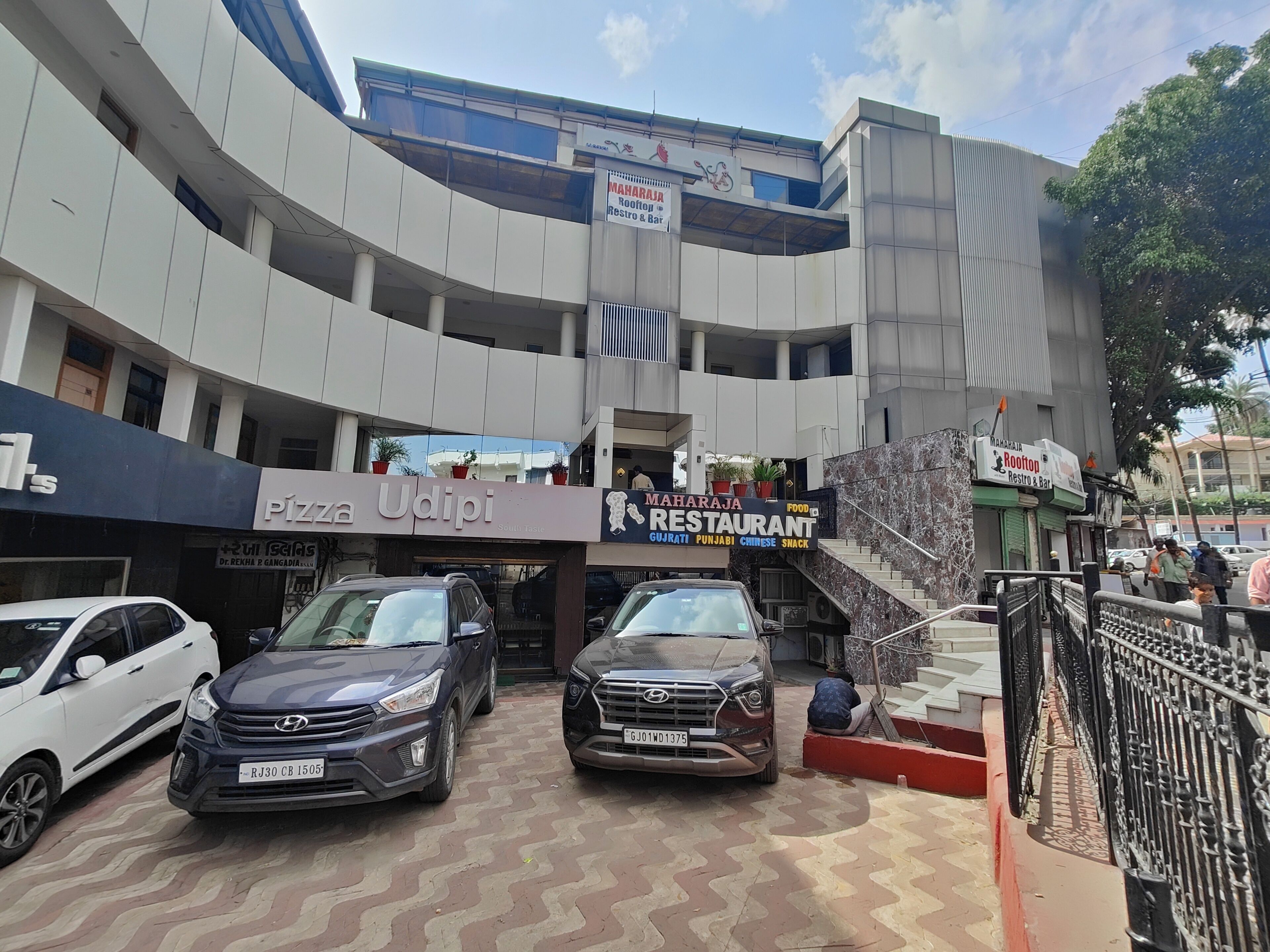 A multi-story building with a restaurant named "MAHARAJI RESTAURANT" and a pizza place called "PIZZA Udipi".