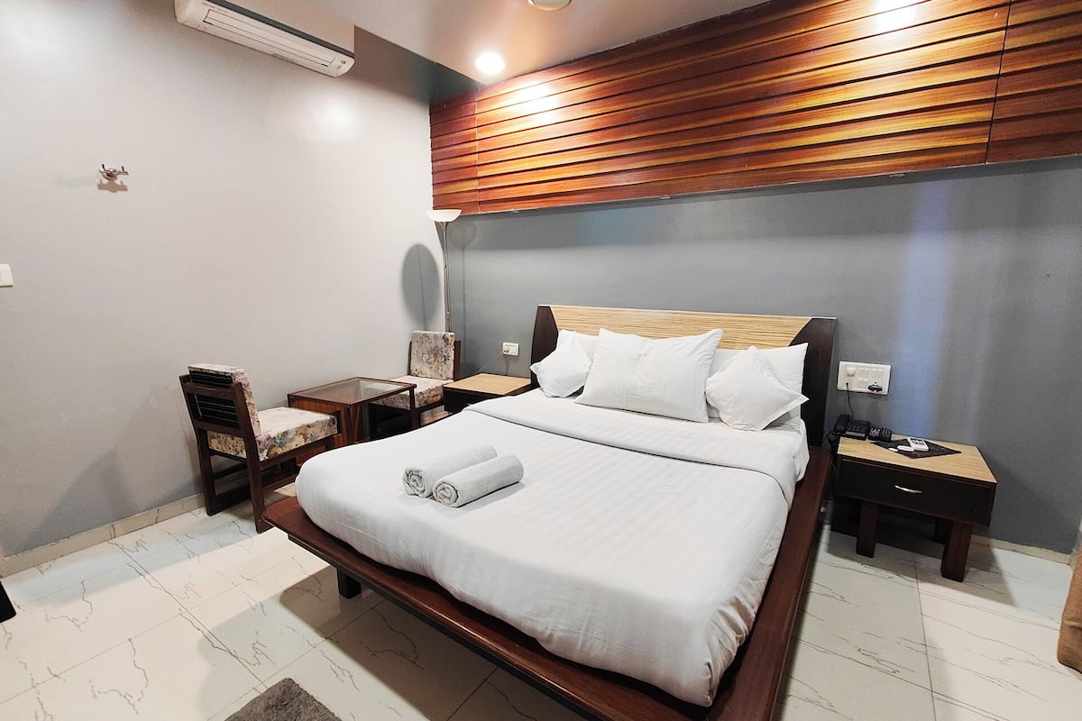 A hotel room with a wooden headboard, a bed with white linens, two nightstands, a lamp, and a chair.