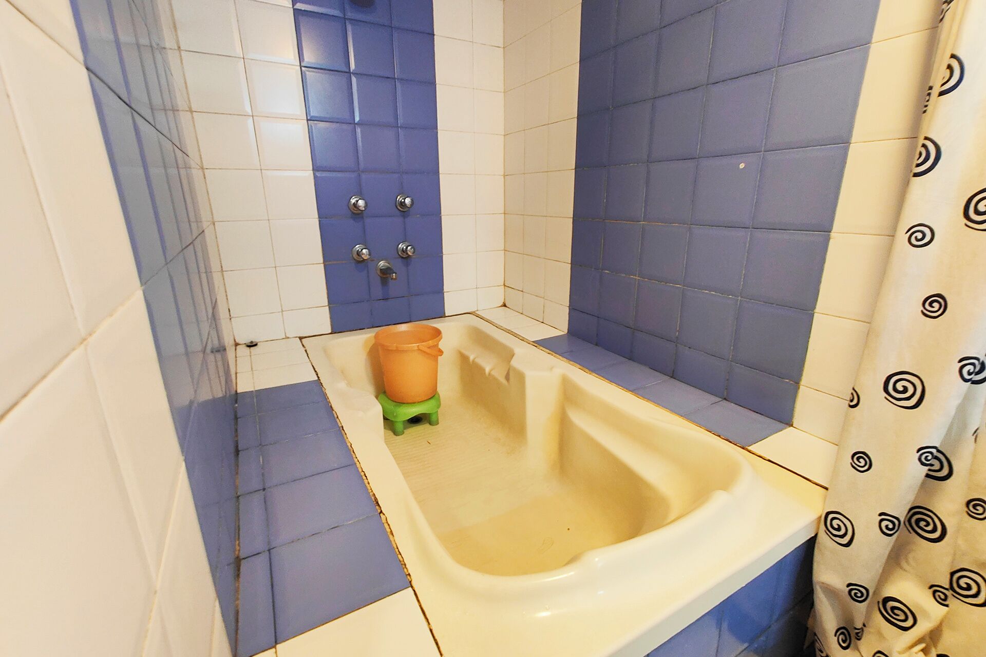 Ein Badezimmer mit einer Badewanne, einem grünen Hocker und einem Duschvorhang mit spiralförmigem Muster.