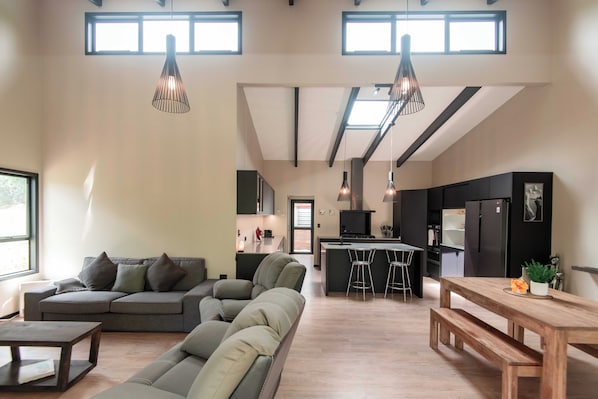 Een ruime woonkamer met een bank, een houten tafel en een keuken op de achtergrond.