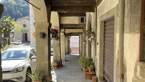 Un passaggio pedonale coperto con piante in vaso, una persiana chiusa a destra e un'auto bianca parcheggiata a sinistra.