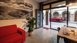 Un interno moderno con un divano rosso, una pianta in vaso, un tavolo da pranzo con bicchieri da vino e vista su un'auto rossa all'esterno.
