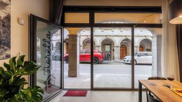 Ein Hotel Eingang mit Glastür, einem Holztisch mit Weingläsern und Blick auf geparkte Autos.