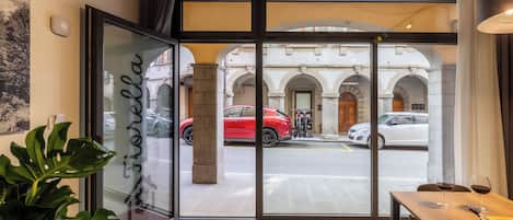 A hotel entrance with a glass door, a wooden table with wine glasses, and a view of parked cars outside.