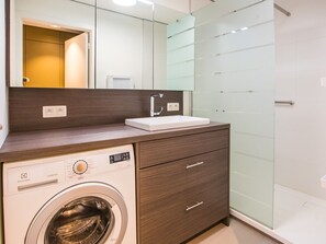 Une salle de bain moderne équipée d’un lave-linge intégré, d’un lavabo et d’une cabine de douche en verre.