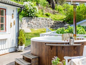A hot tub with wooden steps, a wooden deck, and a stone wall in the background. - 5 Star Holiday Home in Odsmal (Oedsmal)