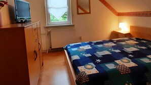Ein Schlafzimmer mit Bett, Schminktisch, Fernseher, Fenster und Nachttisch mit Lampe.